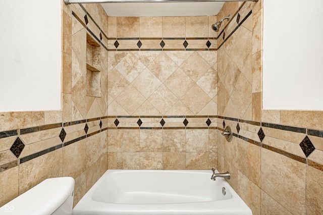 bathroom featuring tiled shower / bath combo, toilet, and tile walls