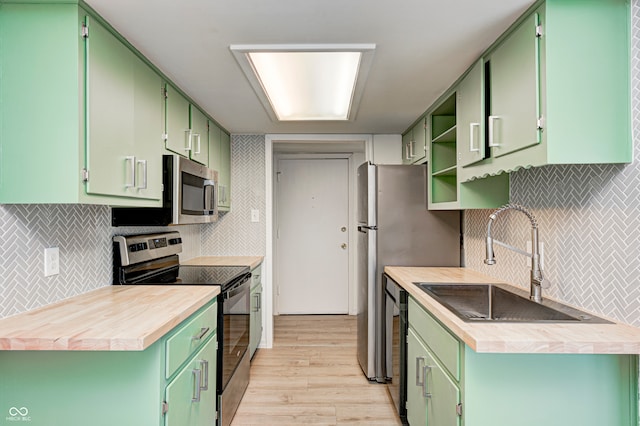 kitchen featuring sink, stainless steel appliances, light hardwood / wood-style flooring, decorative backsplash, and green cabinetry