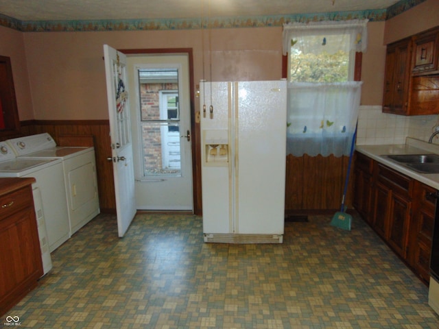 kitchen featuring sink, washing machine and dryer, white refrigerator with ice dispenser, wood walls, and decorative backsplash