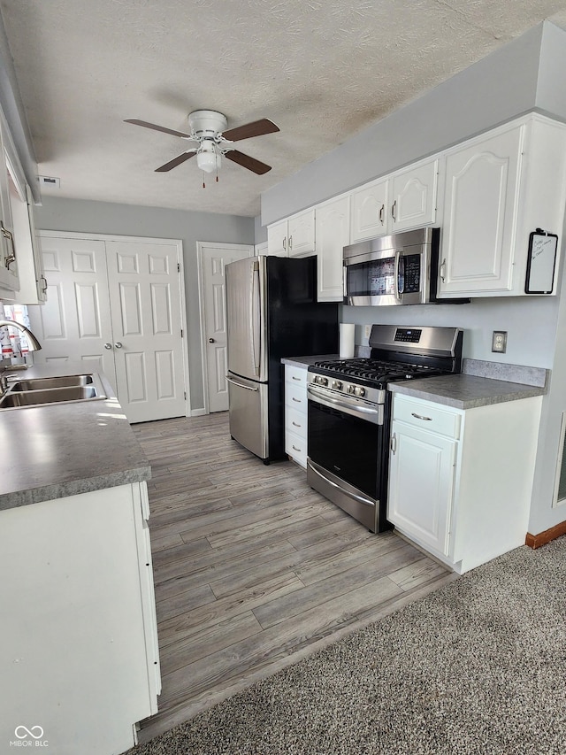 kitchen with sink, a textured ceiling, appliances with stainless steel finishes, ceiling fan, and white cabinets