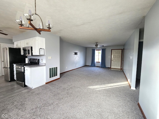 unfurnished living room featuring ceiling fan with notable chandelier, light colored carpet, and a textured ceiling