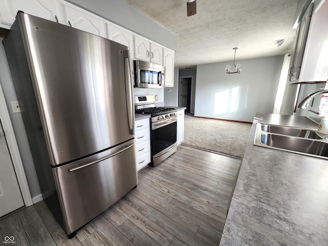 kitchen featuring dark wood-type flooring, sink, hanging light fixtures, stainless steel appliances, and white cabinets