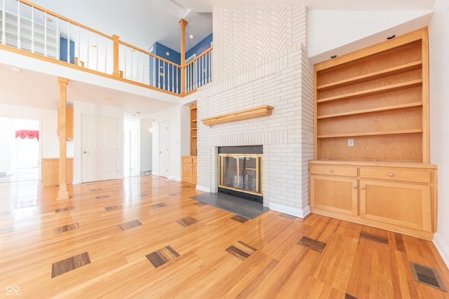 unfurnished living room with built in shelves, light hardwood / wood-style floors, a fireplace, and high vaulted ceiling