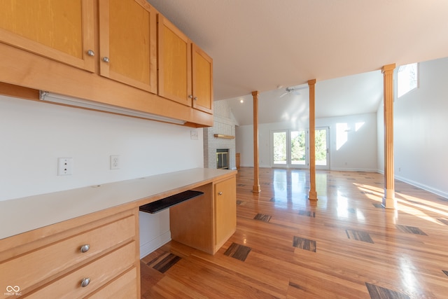 kitchen with light brown cabinets, vaulted ceiling, light hardwood / wood-style flooring, ornate columns, and a fireplace