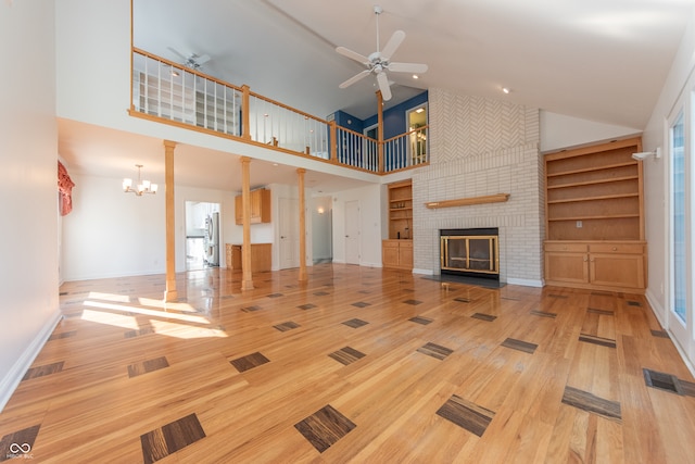 unfurnished living room featuring hardwood / wood-style floors, ceiling fan with notable chandelier, high vaulted ceiling, and a brick fireplace