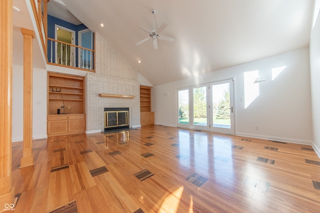 unfurnished living room with light wood-type flooring, a brick fireplace, built in shelves, ceiling fan, and high vaulted ceiling