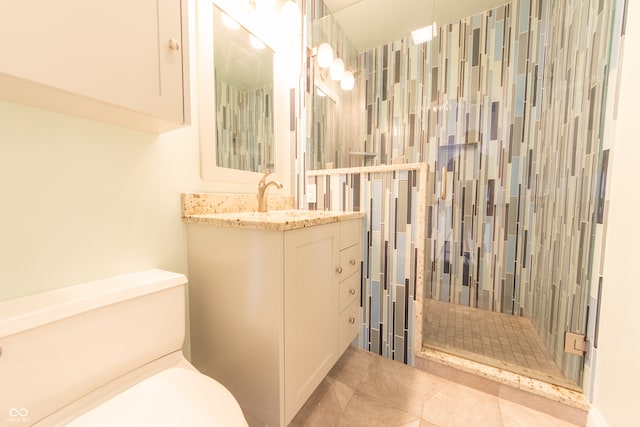 bathroom with tile patterned flooring, vanity, tiled shower, and toilet