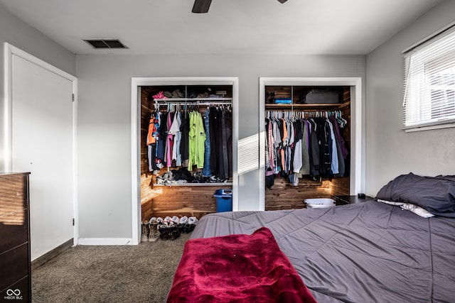 carpeted bedroom with wooden walls, ceiling fan, and multiple closets