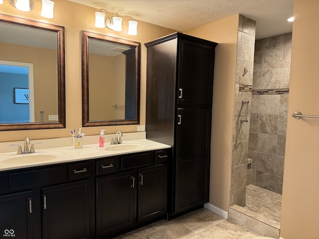 bathroom featuring a textured ceiling, tiled shower, and vanity