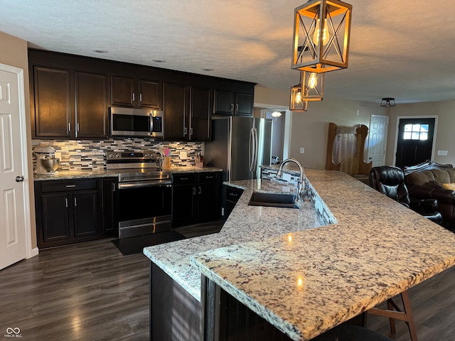 kitchen featuring decorative backsplash, sink, hanging light fixtures, a kitchen island with sink, and appliances with stainless steel finishes