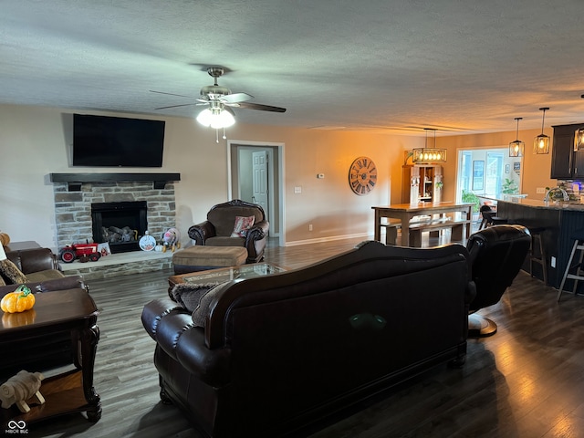 living room with ceiling fan with notable chandelier, a textured ceiling, dark hardwood / wood-style floors, and a fireplace