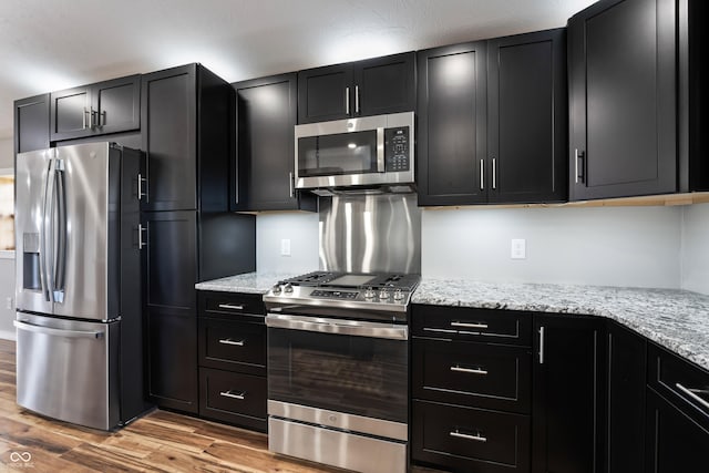9462 N Rushville Rd, Knightstown, IN 46148 - kitchen with stainless steel appliances, dark cabinetry, light wood-type flooring, and light stone counters