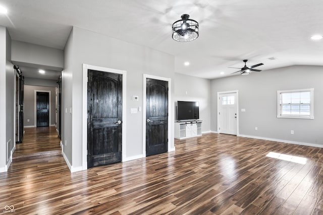 unfurnished living room featuring dark hardwood / wood-style flooring, a barn door, ceiling fan, and lofted ceiling