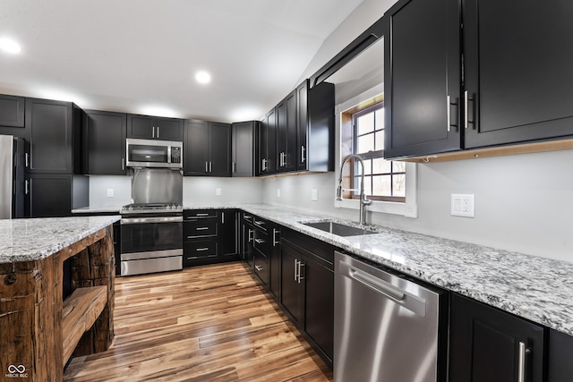 9462 N Rushville Rd, Knightstown, IN 46148 - kitchen with stainless steel appliances, a sink, dark cabinetry, light wood-style flooring, and light stone counters