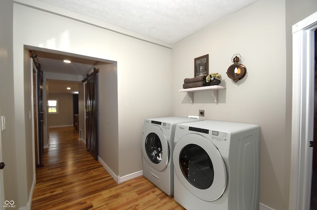 laundry area with a barn door, washer and clothes dryer, wood-type flooring, and a textured ceiling