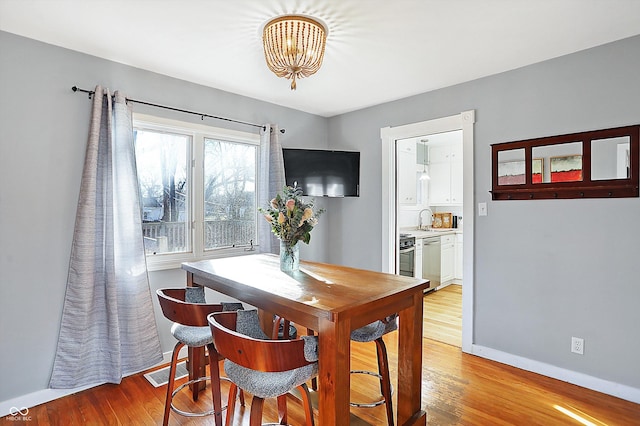 dining area with sink, light hardwood / wood-style floors, and an inviting chandelier