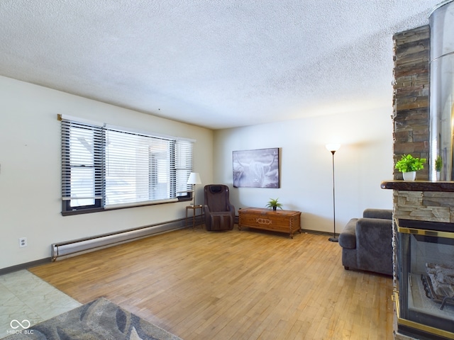 sitting room with baseboard heating, a textured ceiling, light hardwood / wood-style floors, and a stone fireplace