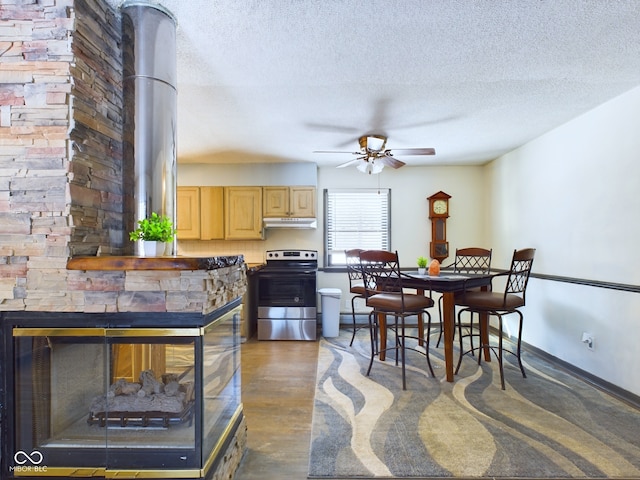 kitchen featuring stainless steel range with electric cooktop, a textured ceiling, ceiling fan, light brown cabinetry, and a stone fireplace