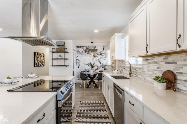 kitchen with island exhaust hood, appliances with stainless steel finishes, light stone counters, white cabinets, and sink