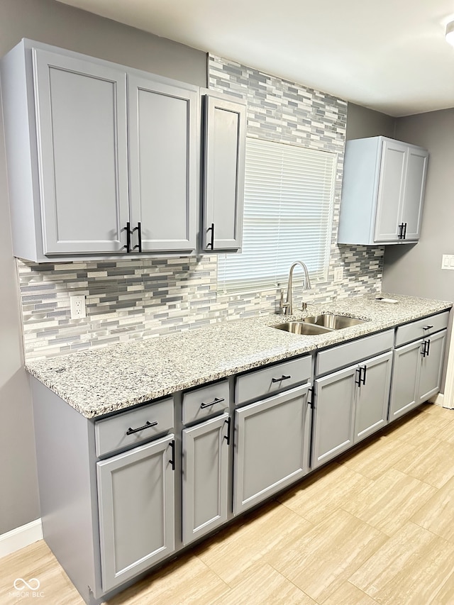 kitchen with light stone countertops, tasteful backsplash, gray cabinets, and sink