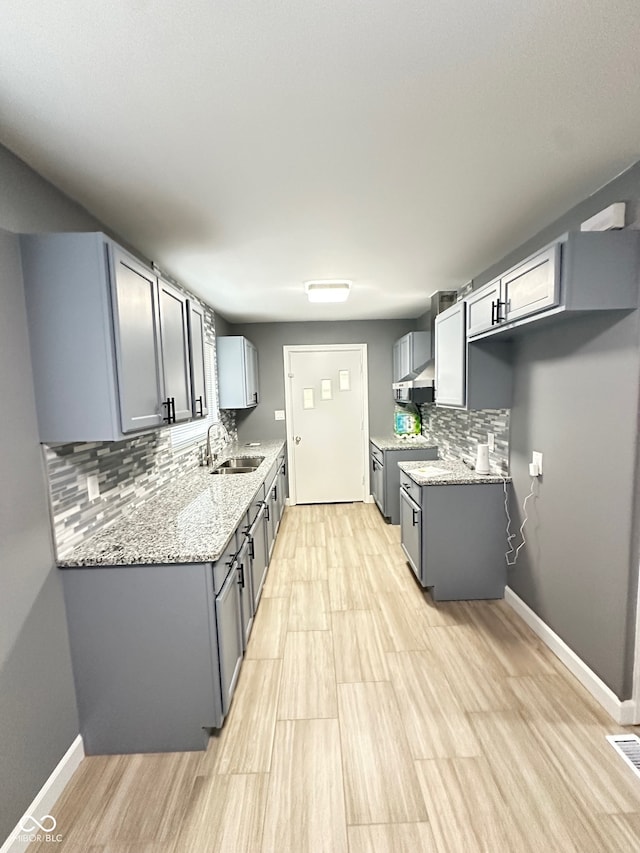 kitchen with sink, stainless steel range, tasteful backsplash, light stone counters, and gray cabinets