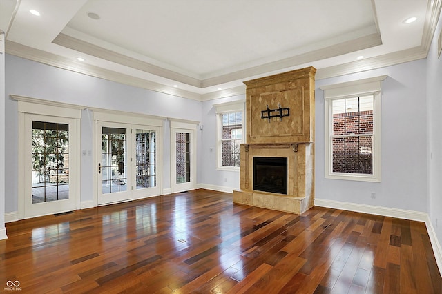 unfurnished living room featuring a raised ceiling, a tiled fireplace, plenty of natural light, and dark wood-type flooring