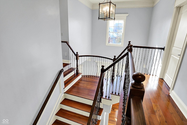 stairway with hardwood / wood-style floors, a notable chandelier, and crown molding