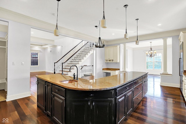 kitchen with ornate columns, sink, a notable chandelier, pendant lighting, and a center island with sink