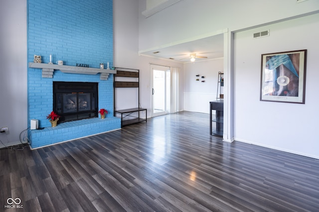 unfurnished living room featuring ceiling fan, a fireplace, a towering ceiling, and dark wood-type flooring