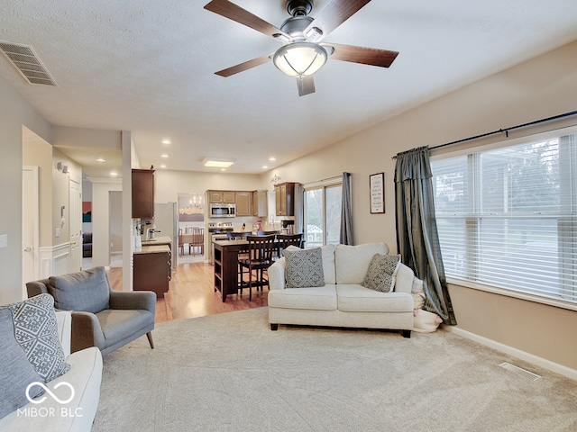 living room featuring ceiling fan, a textured ceiling, and light wood-type flooring