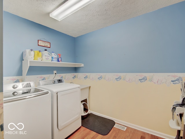 washroom with independent washer and dryer, light wood-type flooring, and a textured ceiling