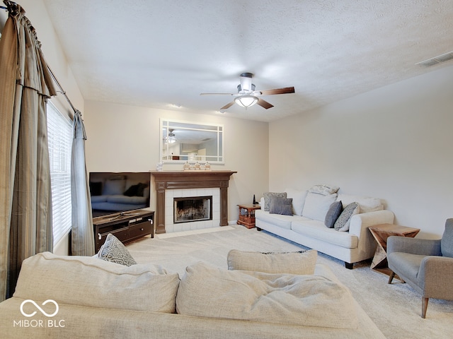 carpeted living room with ceiling fan, a textured ceiling, and a tile fireplace