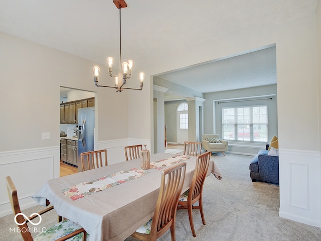 dining area with a notable chandelier, light colored carpet, and ornate columns