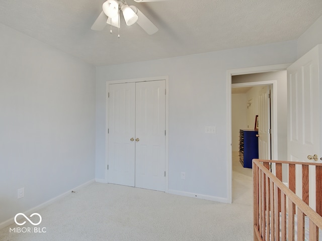 unfurnished bedroom featuring a textured ceiling, light colored carpet, a closet, and ceiling fan