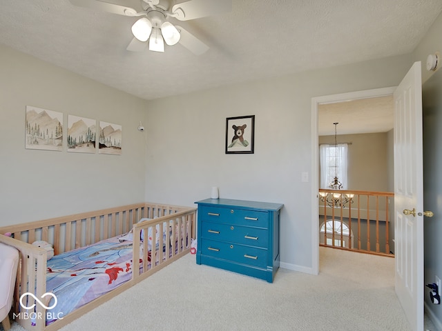 bedroom featuring ceiling fan with notable chandelier, light colored carpet, and a textured ceiling