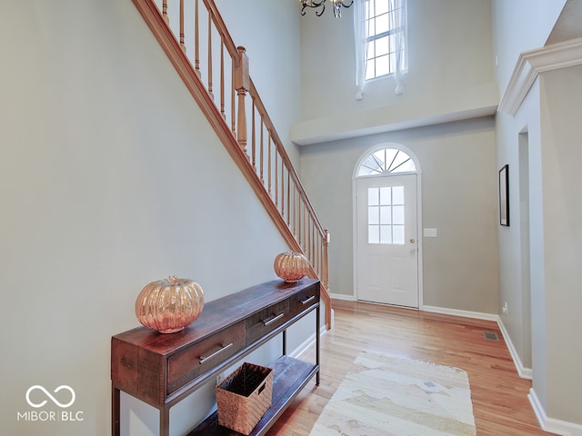 foyer featuring a towering ceiling, light wood-type flooring, and an inviting chandelier