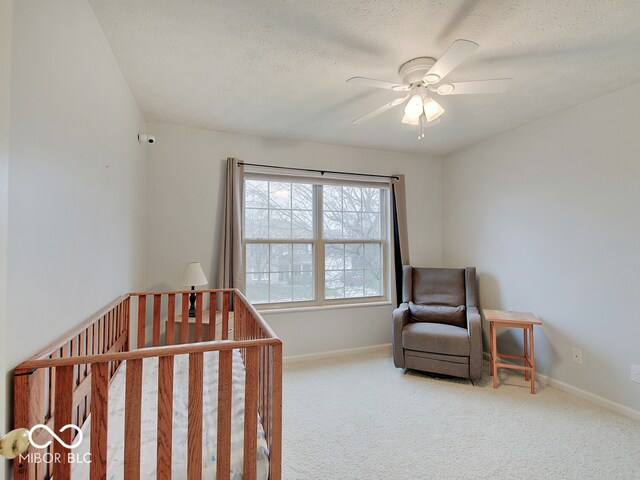 bedroom with a crib, a textured ceiling, carpet floors, and ceiling fan