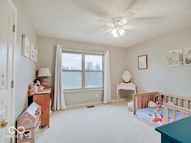 carpeted bedroom with a textured ceiling, ceiling fan, and a crib