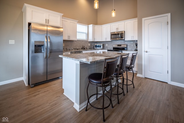 kitchen featuring hanging light fixtures, a kitchen island, dark hardwood / wood-style flooring, white cabinetry, and stainless steel appliances