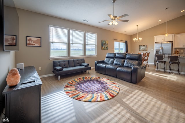 living room with ceiling fan with notable chandelier, light hardwood / wood-style floors, and vaulted ceiling