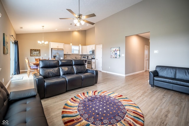 living room with ceiling fan with notable chandelier, light wood-type flooring, and high vaulted ceiling