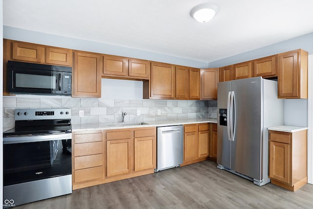 kitchen with tasteful backsplash, sink, light wood-type flooring, and appliances with stainless steel finishes