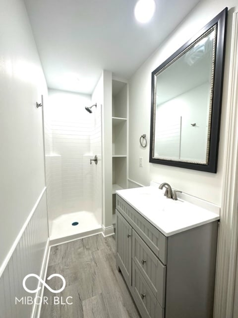 bathroom with a tile shower, vanity, and wood-type flooring