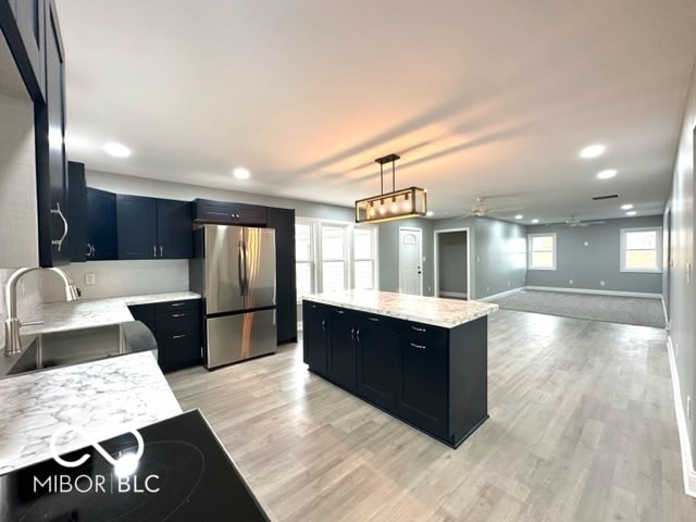 kitchen with light wood-type flooring, ceiling fan, sink, pendant lighting, and stainless steel refrigerator