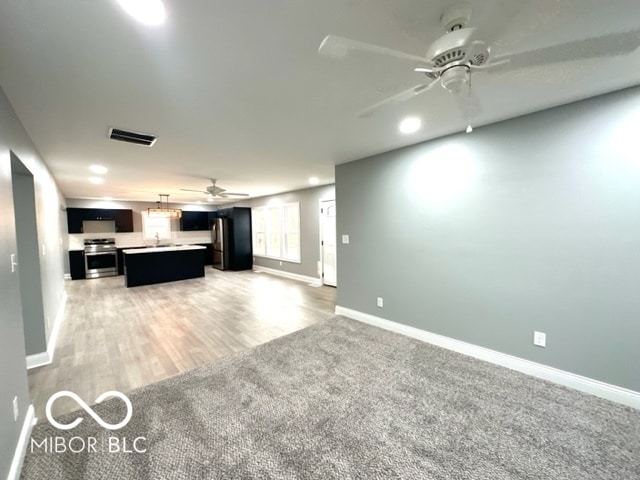 unfurnished living room featuring ceiling fan and light colored carpet