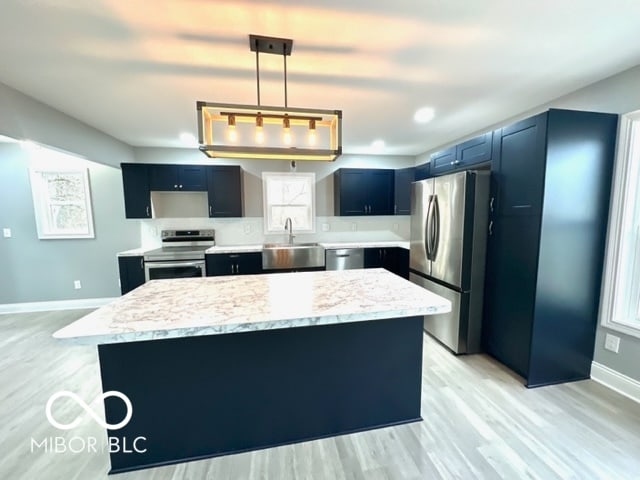 kitchen featuring a center island, sink, hanging light fixtures, light wood-type flooring, and stainless steel appliances