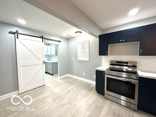 kitchen with stainless steel electric range oven, light stone countertops, tasteful backsplash, a barn door, and light hardwood / wood-style flooring