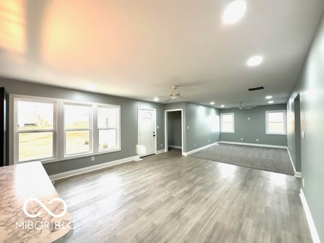 unfurnished living room with wood-type flooring, a wealth of natural light, and ceiling fan