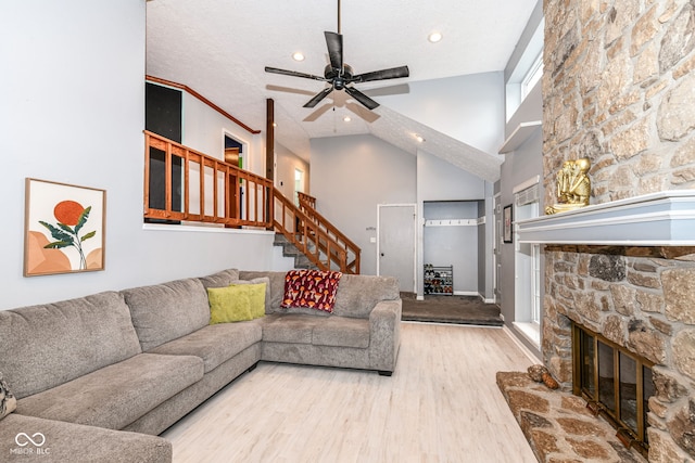 living room featuring hardwood / wood-style floors, a stone fireplace, a textured ceiling, and high vaulted ceiling