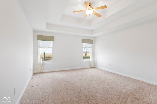 carpeted empty room with a raised ceiling and ceiling fan